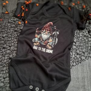 A flat lay of a black baby bodysuit featuring a biker gnome with a plaid hat, tattoos, and a chopper motorcycle, along with the text "Bad to the Gnome." Perfect for biker families and a unique baby shower gift for motorcycle enthusiasts.