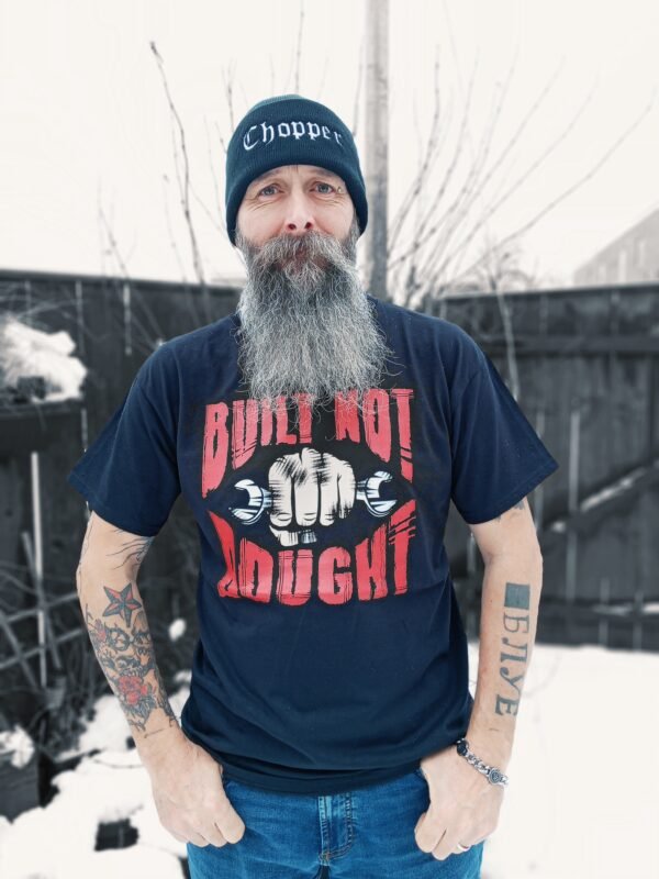 Man wearing a black 'Built Not Bought' T-shirt with bold red and white graphic, standing outdoors in a snowy background