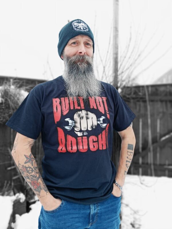 Man wearing a black 'Built Not Bought' T-shirt with bold red and white graphic, standing outdoors in a snowy background