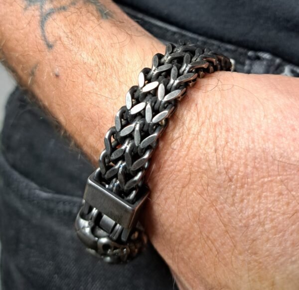 Close-up of the stainless steel skull biker bracelet, highlighting cracked skull accents and the dark gunmetal finish and slide-lock clasp.
