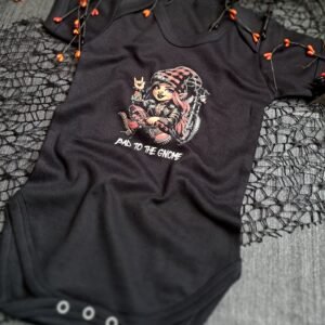 An angled view of the Girlie "Bad to the Gnome" black baby vest, featuring a pink-haired biker gnome sitting next to a chopper motorcycle, with autumn-themed décor surrounding the vest.