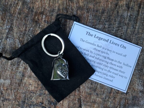 "Lady biker stainless steel guardian angel gremlin bell keychain displayed with a black velvet pouch and legend card explaining the protective purpose of the bell, photographed on a wooden background.