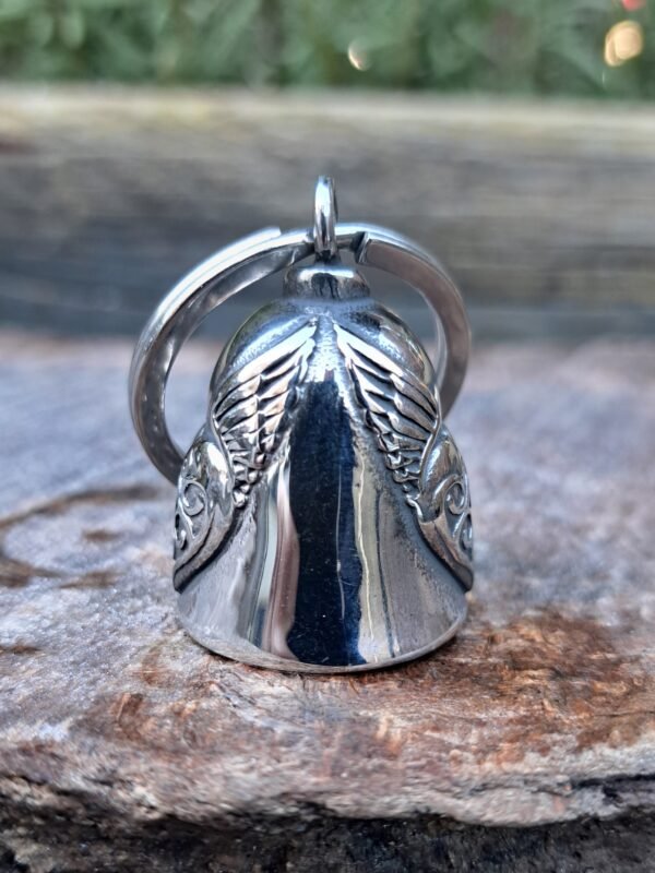 "Side view of a lady biker stainless steel motorbike gremlin bell keychain with intricate wing and heart pattern, displayed on a rustic surface.