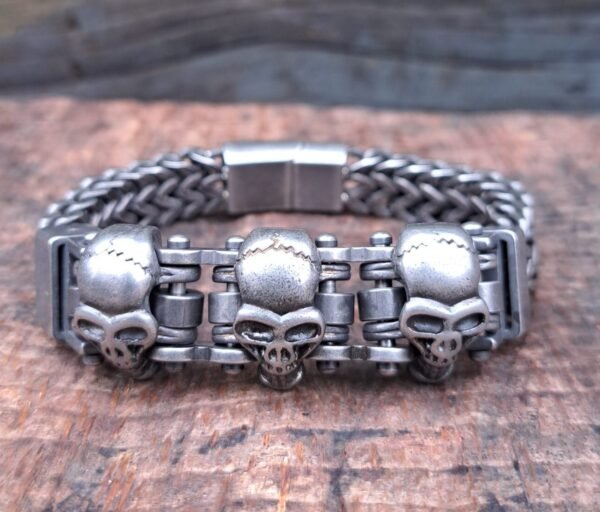 Stainless steel skull biker bracelet with a rugged chain design and oxidized skull accents, displayed on a wooden surface.