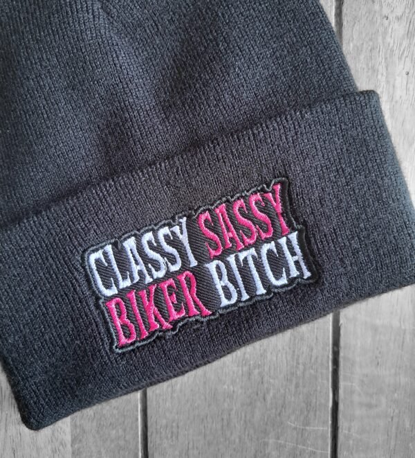 Close-up of pink and white stitched text on black knit beanie