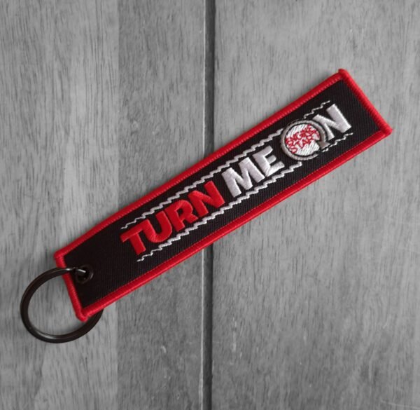 Red and black Engine Start Keychain embroidered keytag with "TURN ME ON" text and engine start button graphic – front view