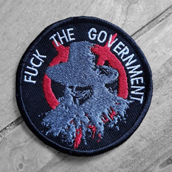 Round embroidered patch with stylized Guy Fawkes design and the words "Fuck the Government" in white thread, angled view.