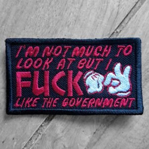 Embroidered patch with red and white text reading “I’m not much to look at but I f*ck like the government” on dark fabric, angled view.
