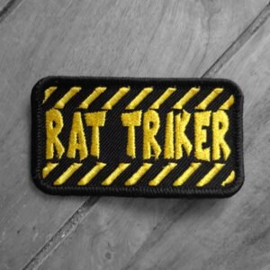 Embroidered “Rat Triker” patch with bold yellow text on black background and diagonal hazard-style stripes.