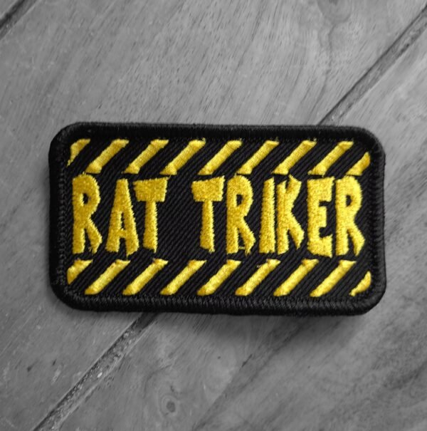 Embroidered “Rat Triker” patch with bold yellow text on black background and diagonal hazard-style stripes.