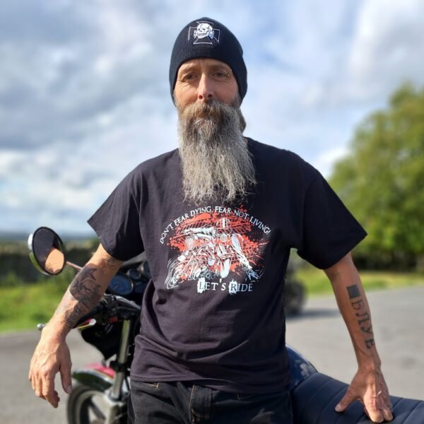 Person wearing black biker t-shirt with “Don’t Fear Dying, Fear Not Living! Let’s Ride” design, standing by a motorcycle.