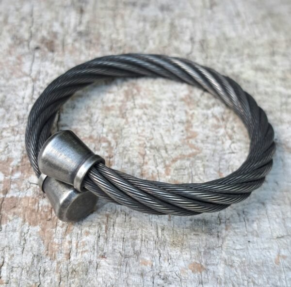 Stainless steel cable biker bracelet with tapered end caps on wood; 9mm cable, 13mm tips.