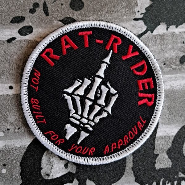 Angled close-up of a RAT-RYDER biker patch showing a white skeleton hand flipping the middle finger with red lettering that says ‘Not built for your approval.