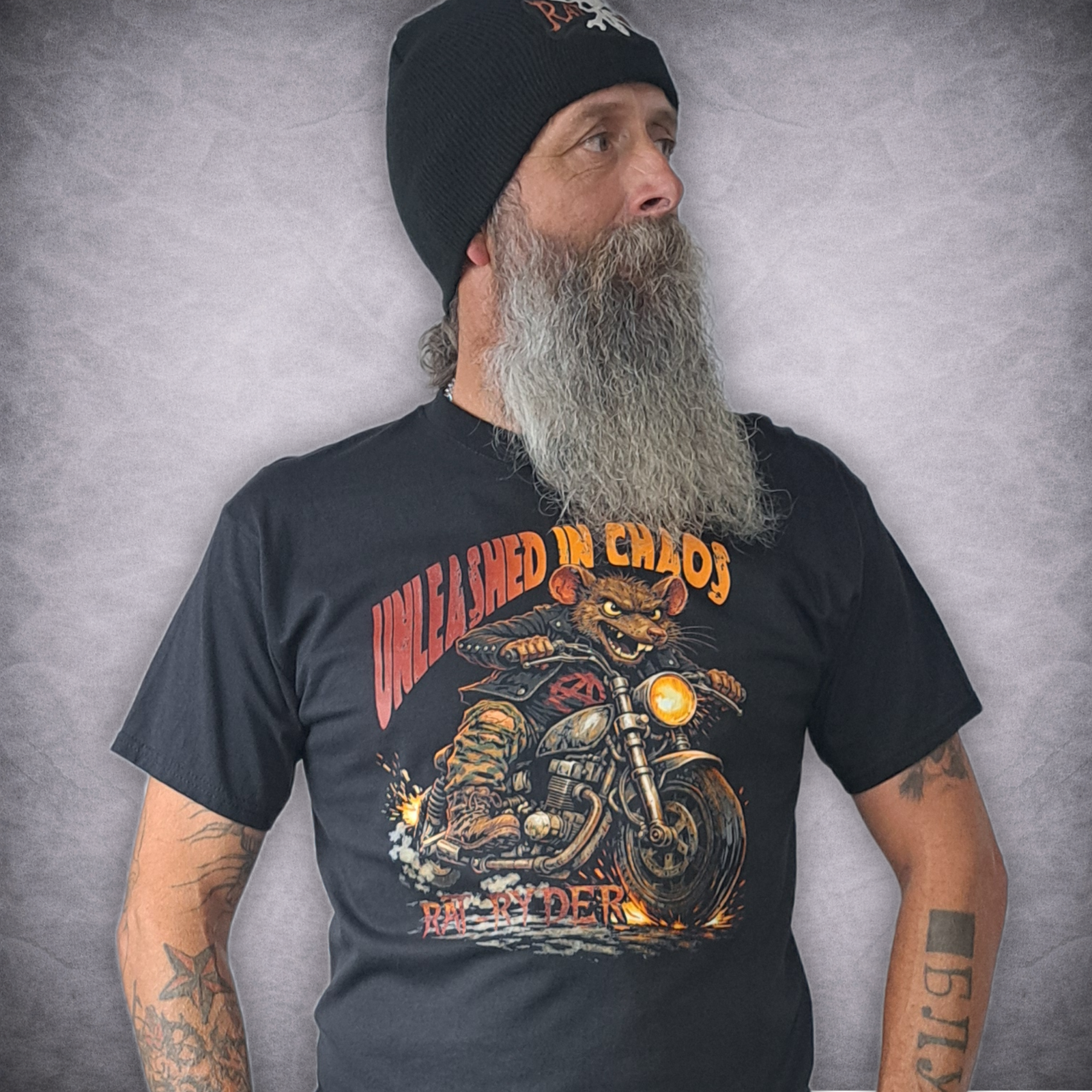 Rat-Ryder 'Lou the Rat - Unleashed in Chaos Black T-Shirt 1 Man with long beard wearing black Rat-Ryder t-shirt featuring Lou the Rat riding a motorcycle out of flames with red and orange Unleashed in Chaos typography.
