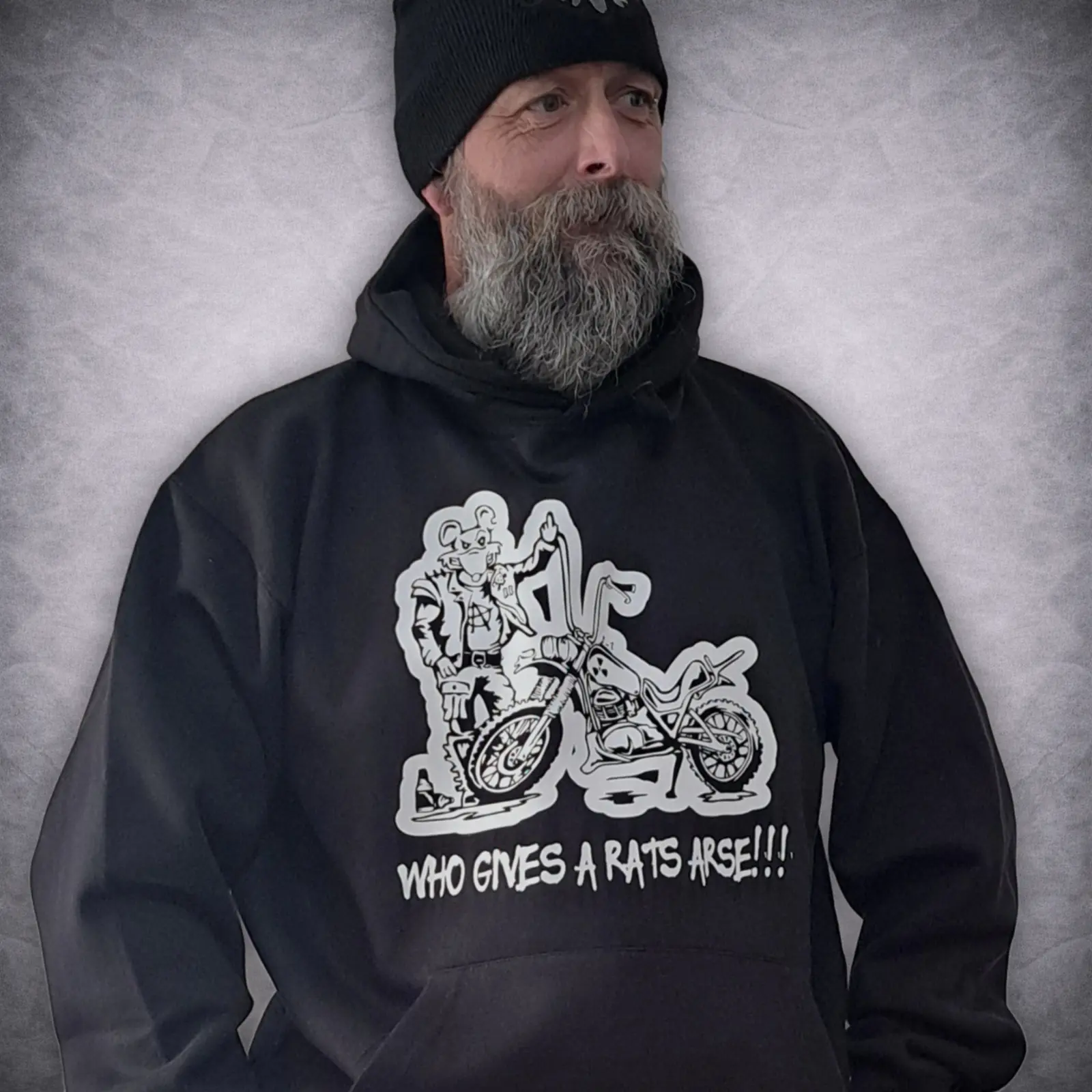 Who Gives A Rats Arse Rat Bike Hoodie 1 Side angle of a bearded man looking away, wearing a black biker hoodie with a cartoon motorcycle rat graphic.