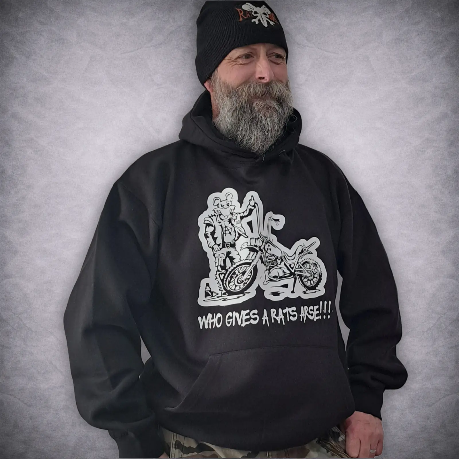 Who Gives A Rats Arse Rat Bike Hoodie 2 Bearded man wearing a black biker hoodie featuring a white "Who Gives A Rats Arse" cartoon rat and motorcycle graphic.